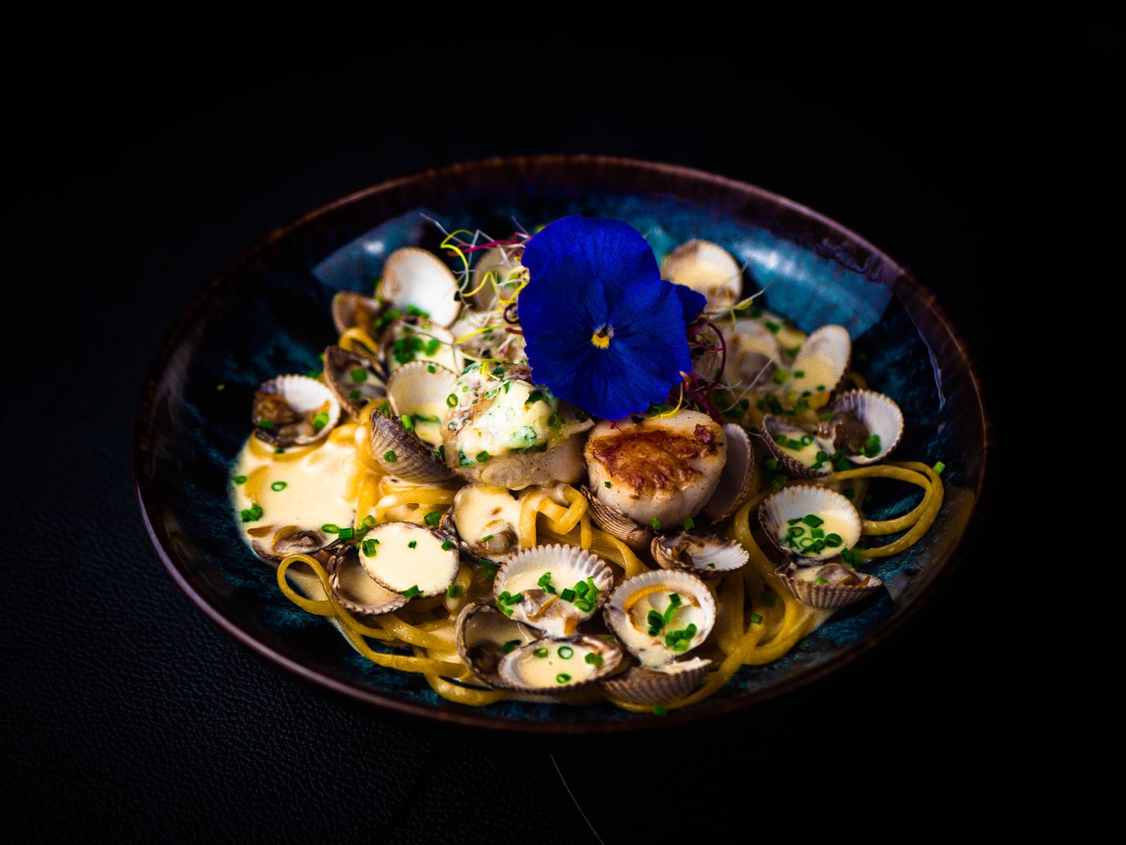 Assiette de pâtes aux coquillages dressée avec une fleur bleue.