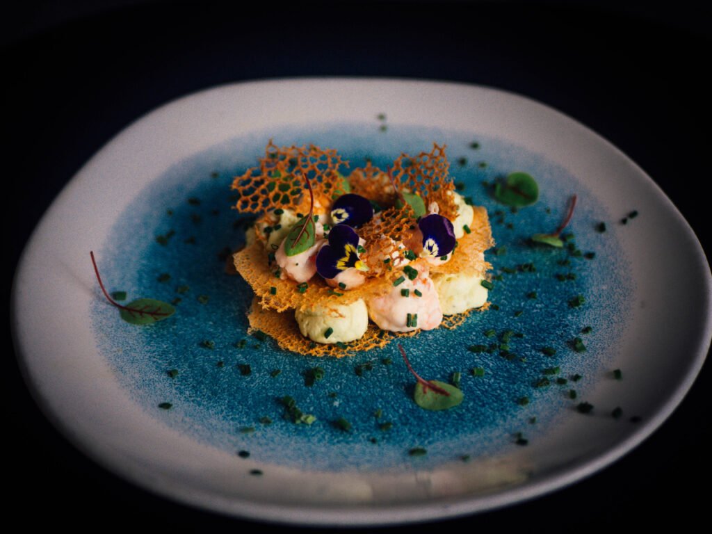 Assiette bleu profond, dressage coloré et fleurs violettes.